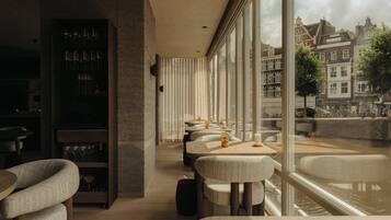 A modern interior with a bar area, seating, and a view of a canal with buildings.