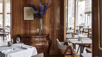 Un restaurant avec des murs lambrés, un vase rempli de fleurs violettes et des tables dressées pour le dîner.
