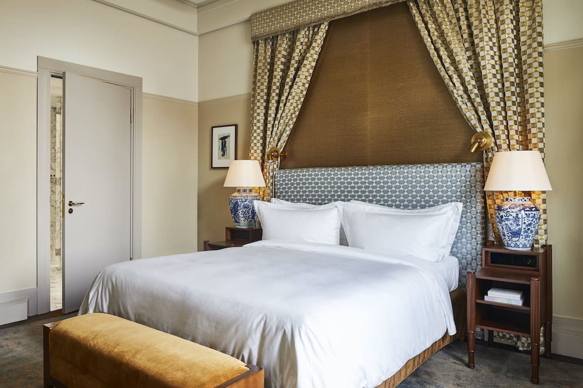 Een hotelkamer met een groot bed, twee nachtkastjes met lampen, een houten bankje en een deur.