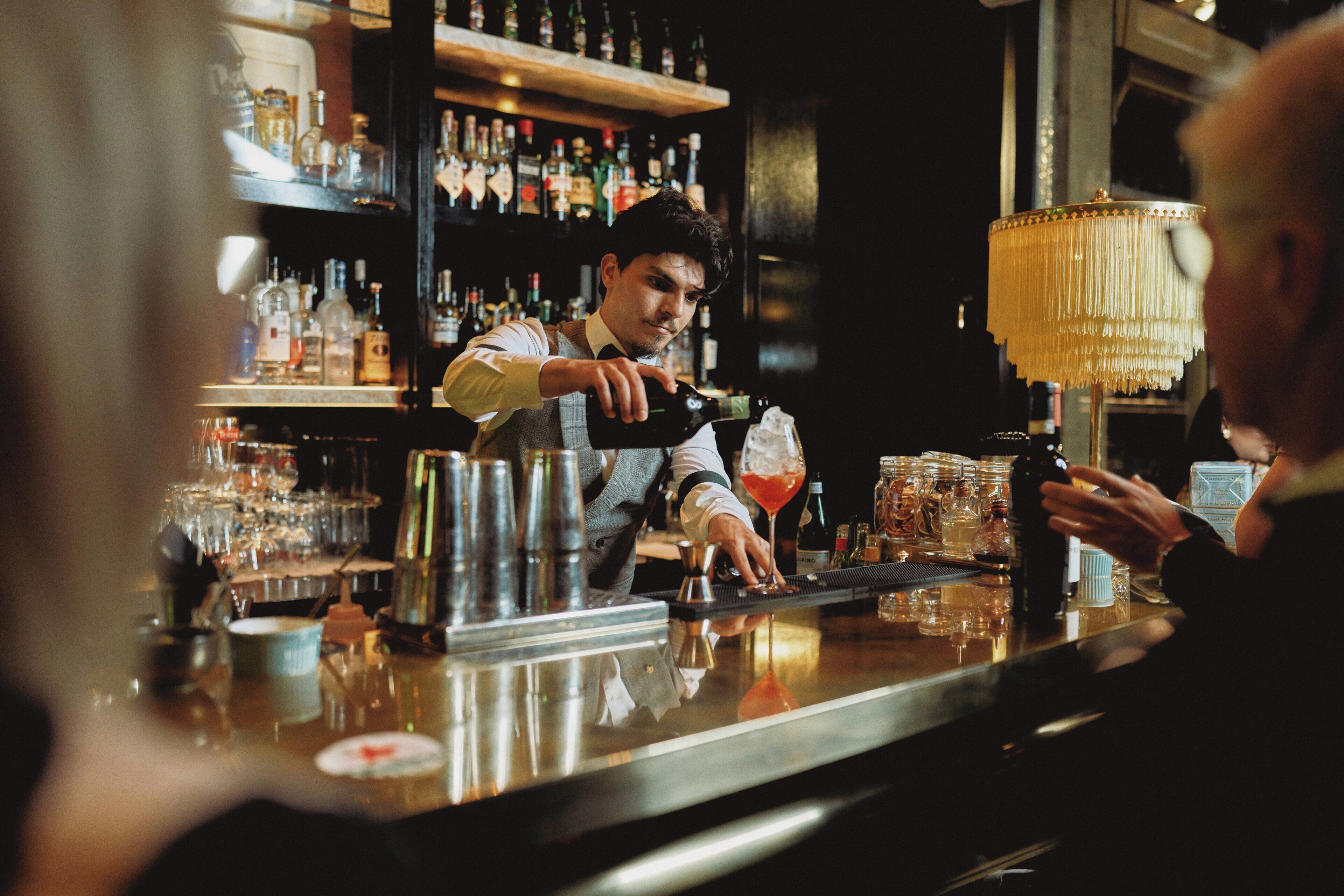 A bar with a bartender preparing a drink, shelves with bottles, and a bar counter.