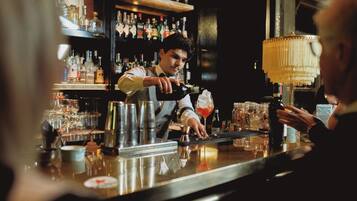 A bar with a bartender preparing a drink, shelves with bottles, and a bar counter.