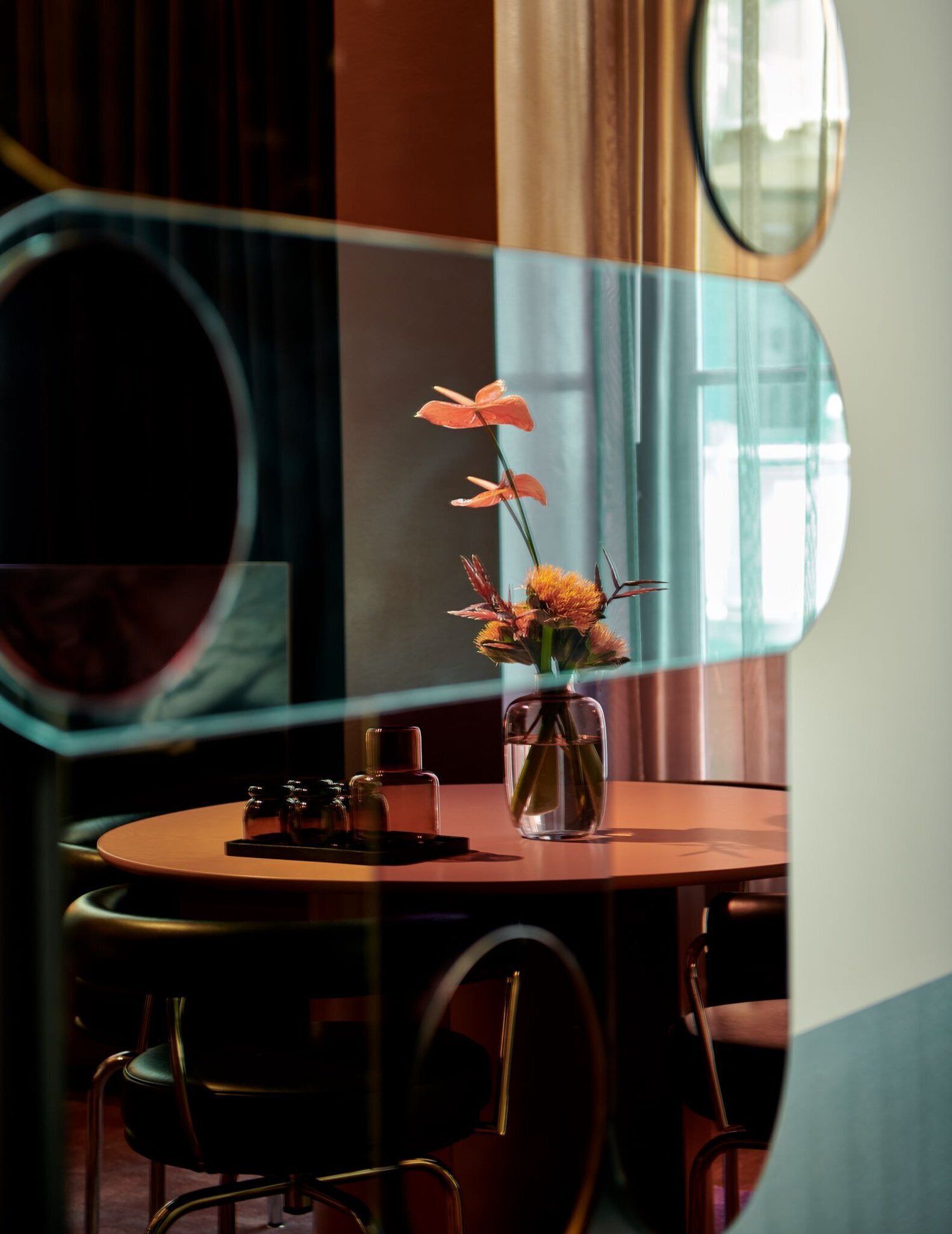 A dining table with a vase of flowers, a small tray with condiments, and a mirror reflecting the room.