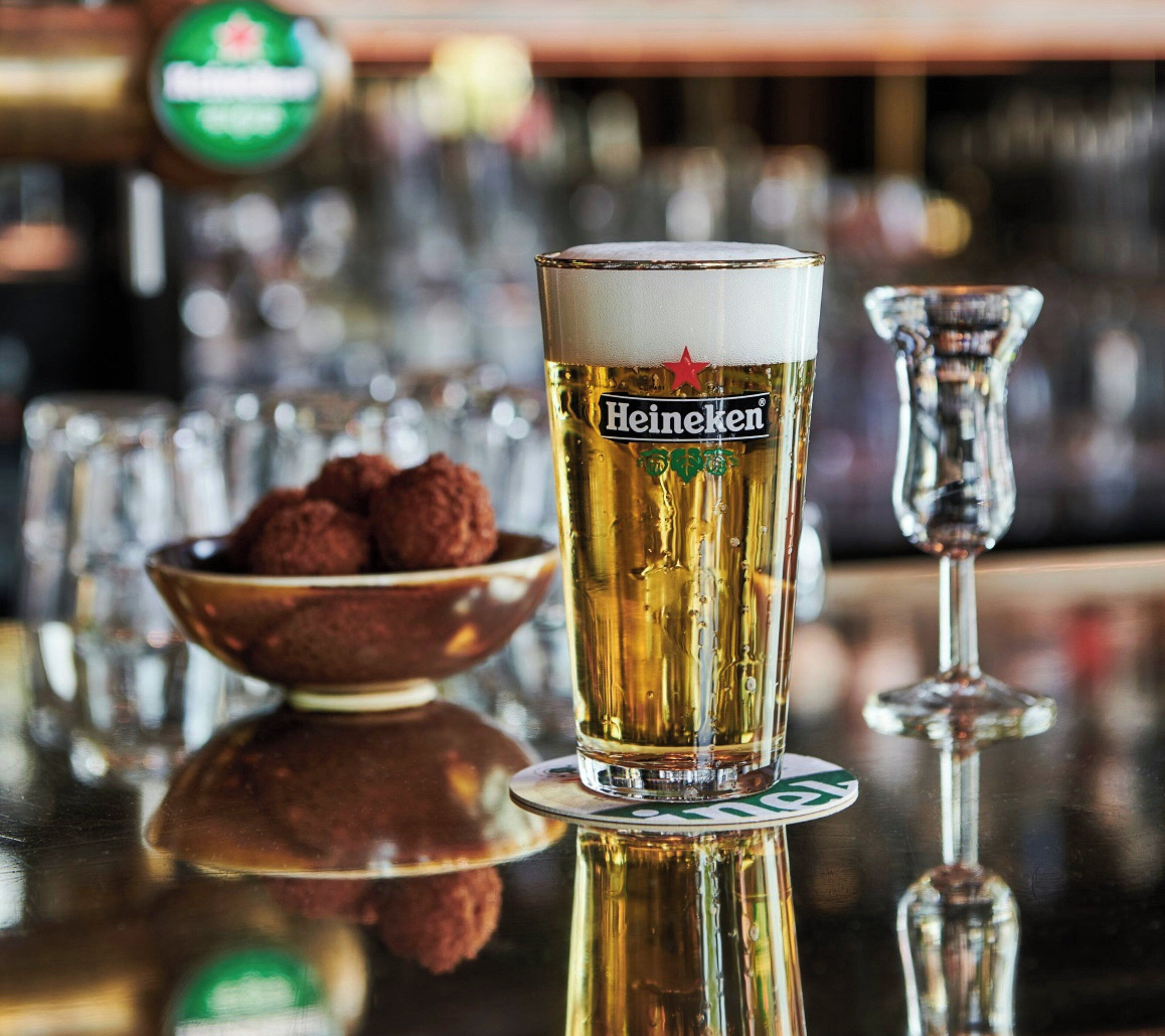 Um copo de Heineken sobre um apoio com uma taça de chocolates ao fundo.