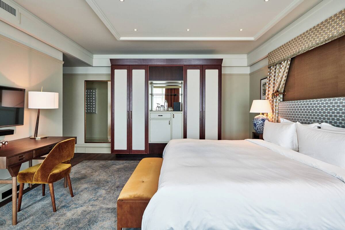 A hotel room with a large bed, a desk with a chair, a television, and a wardrobe.
