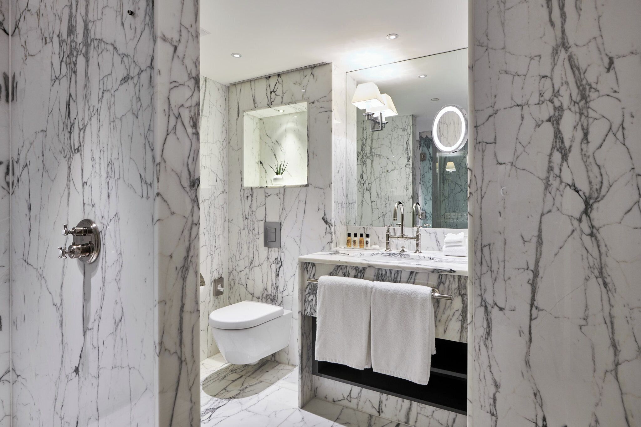 A modern bathroom with a marble floor, a toilet, a sink with a mirror, and a shower area.