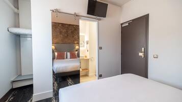 A hotel room with a bed, a TV mounted on the wall, a door, and a bathroom visible through an open door.