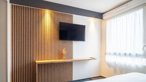 Une chambre d’hôtel moderne avec un mur en lambris de bois, un téléviseur à écran plat fixé au mur et une table de chevet agrémentée d’un vase.