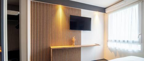 Habitación de hotel moderna con pared de listones de madera, un televisor de pantalla plana montado y una mesita de noche con un florero.