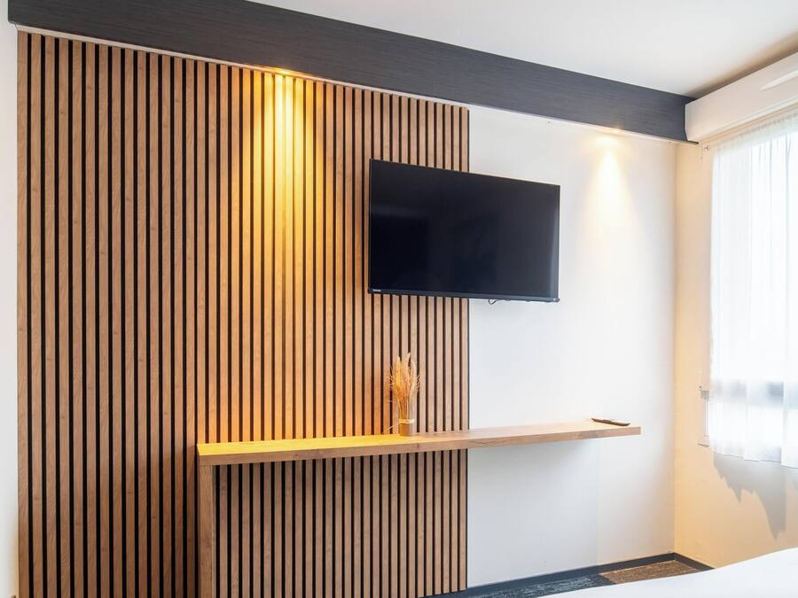 Habitación de hotel moderna con pared de listones de madera, un televisor de pantalla plana montado y una mesita de noche con un florero.