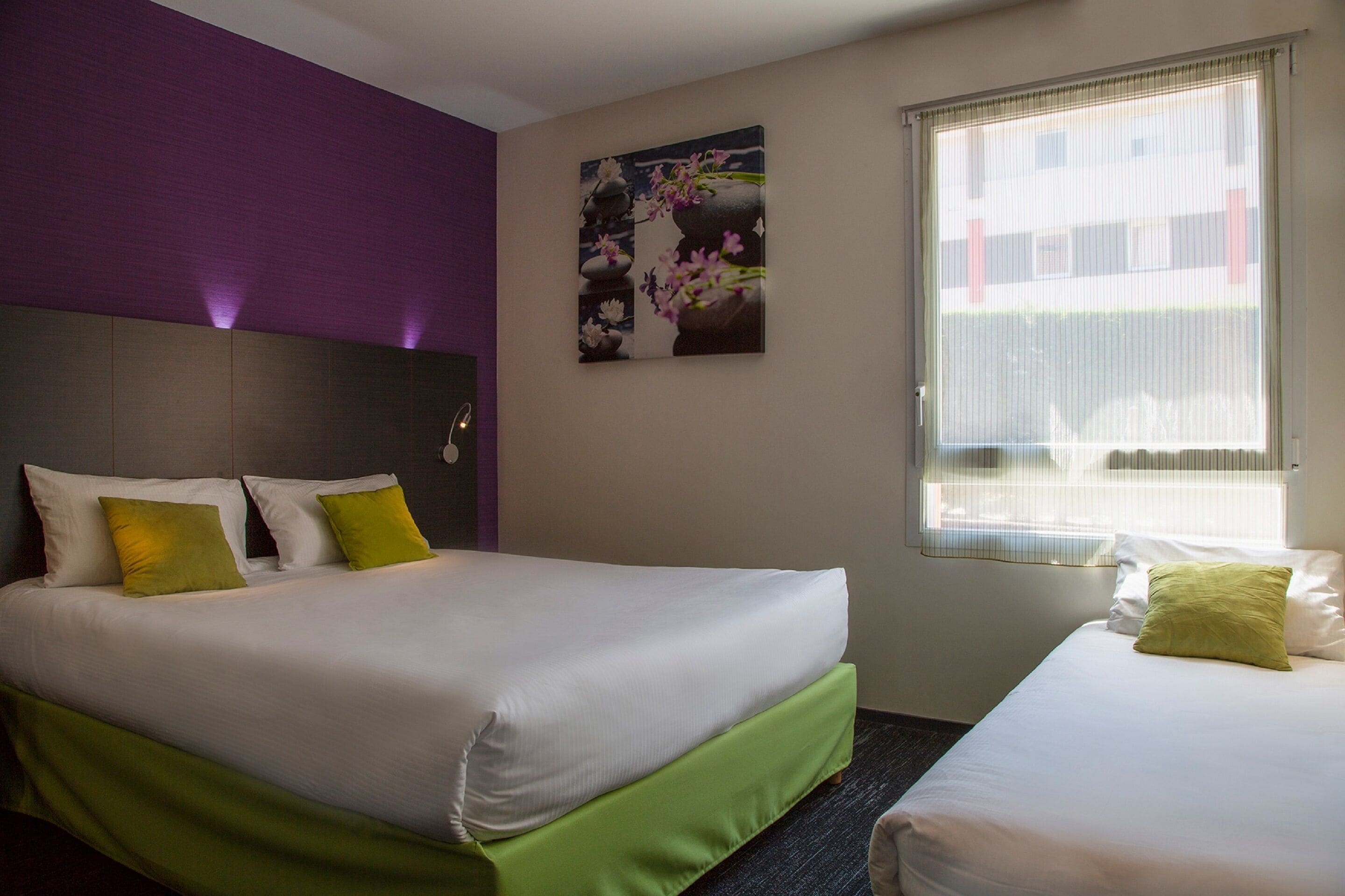 Une chambre d’hôtel avec un grand lit, un lit plus petit, une fenêtre avec des stores et une œuvre d’art accrochée au mur.