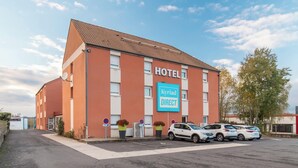 Un hôtel dont la façade porte une enseigne indiquant « HÔTEL » et « Kyriad DIRECT ». Trois voitures sont garées devant.