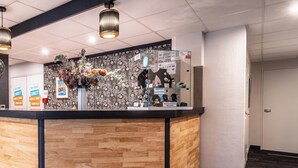 Un comptoir d’accueil agrémenté d’un arrangement floral, d’une horloge et d’une enseigne indiquant « Kyriad Direct ».