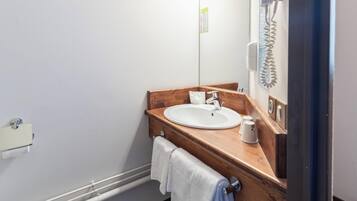 Un baño con tocador de madera, un lavabo blanco, un espejo, un perchero para toallas y un secador de manos.