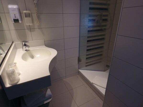 Un baño con un lavamanos blanco, un espejo, un dispensador de jabón manual y un vaso con desinfectante de manos.