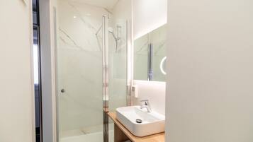A modern bathroom with a glass-enclosed shower, a white sink, and a mirror with a circular light.