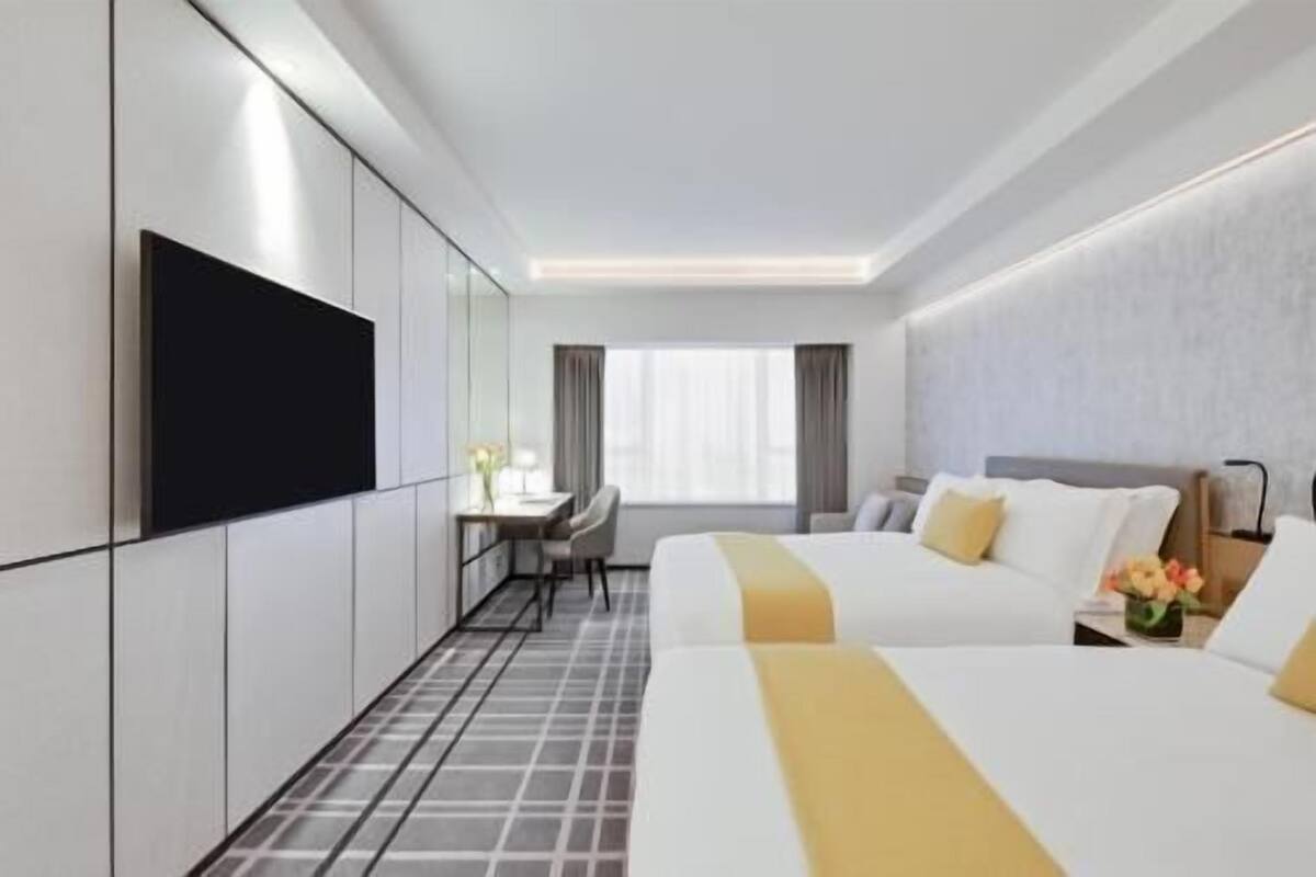 Une chambre d’hôtel avec deux lits, un bureau, une chaise, une télévision et une fenêtre.