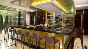 A modern bar area with a glass partition, bar stools, and a variety of bottles and glasses on shelves. - Royal Park Hotel (Sha Tin)