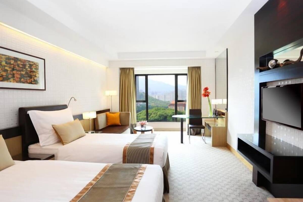 Une chambre d’hôtel avec deux lits, un bureau, une télévision et une vue sur la verdure.