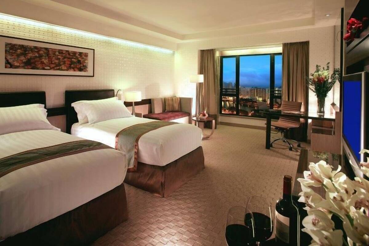 Une chambre d’hôtel avec deux lits, un bureau, une chaise, une télévision et une grande fenêtre donnant sur la ville.