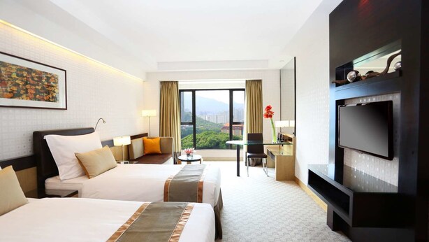 A hotel room with two beds, a desk, a TV, and a view of the city. - Royal Park Hotel (Sha Tin)