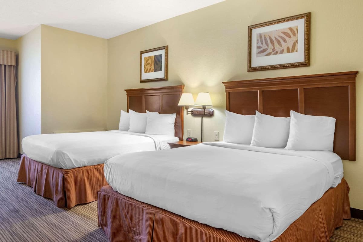 A hotel room with two beds, a wooden headboard, a nightstand with a lamp, and two framed pictures on the wall.