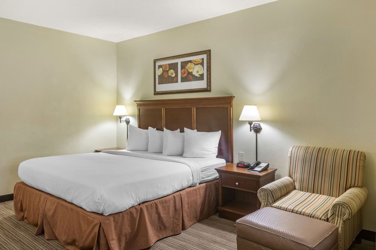 A hotel room with a large bed, two bedside tables with lamps, a chair, and a framed picture on the wall.