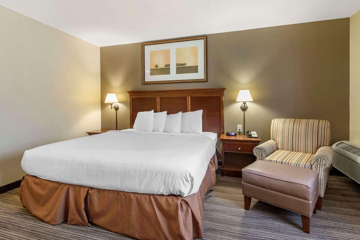 A hotel room with a large bed, two bedside lamps, a chair, a small table, and a framed picture on the wall.
