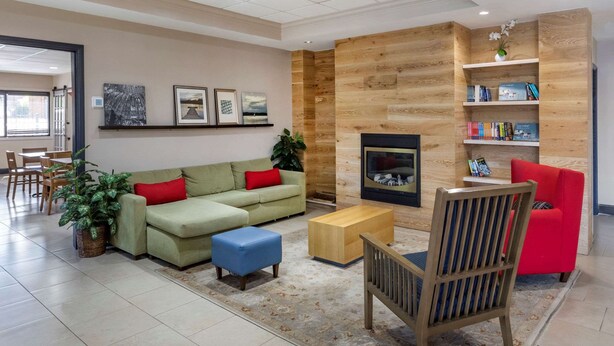 A modern living room with a sofa, ottoman, and a red chair. There is a fireplace, a bookshelf, and a dining area in the background. - Country Inn & Suites by Radisson, Atlanta Downtown (Atlanta)