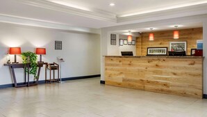 A reception area with a wooden reception desk, two red pendant lights, framed pictures on the wall, and a small plant on a table. - Country Inn & Suites by Radisson, Atlanta Downtown (Atlanta)