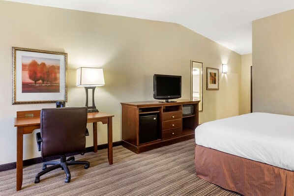 A hotel room with a bed, desk, chair, television, and a lamp.