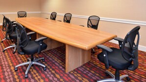 A conference room with a long wooden table, six black office chairs with mesh backs, and a patterned carpet. - Holiday Inn New London - Mystic Area by IHG (New London)