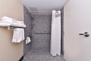 A modern shower area with a tiled wall, a metal towel rack with folded towels, and a shower curtain. - Holiday Inn New London - Mystic Area by IHG (New London)
