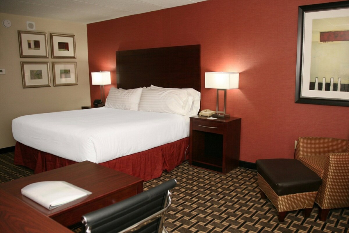 A hotel room with a large bed, two bedside tables, a desk, a chair, and a patterned carpet.
