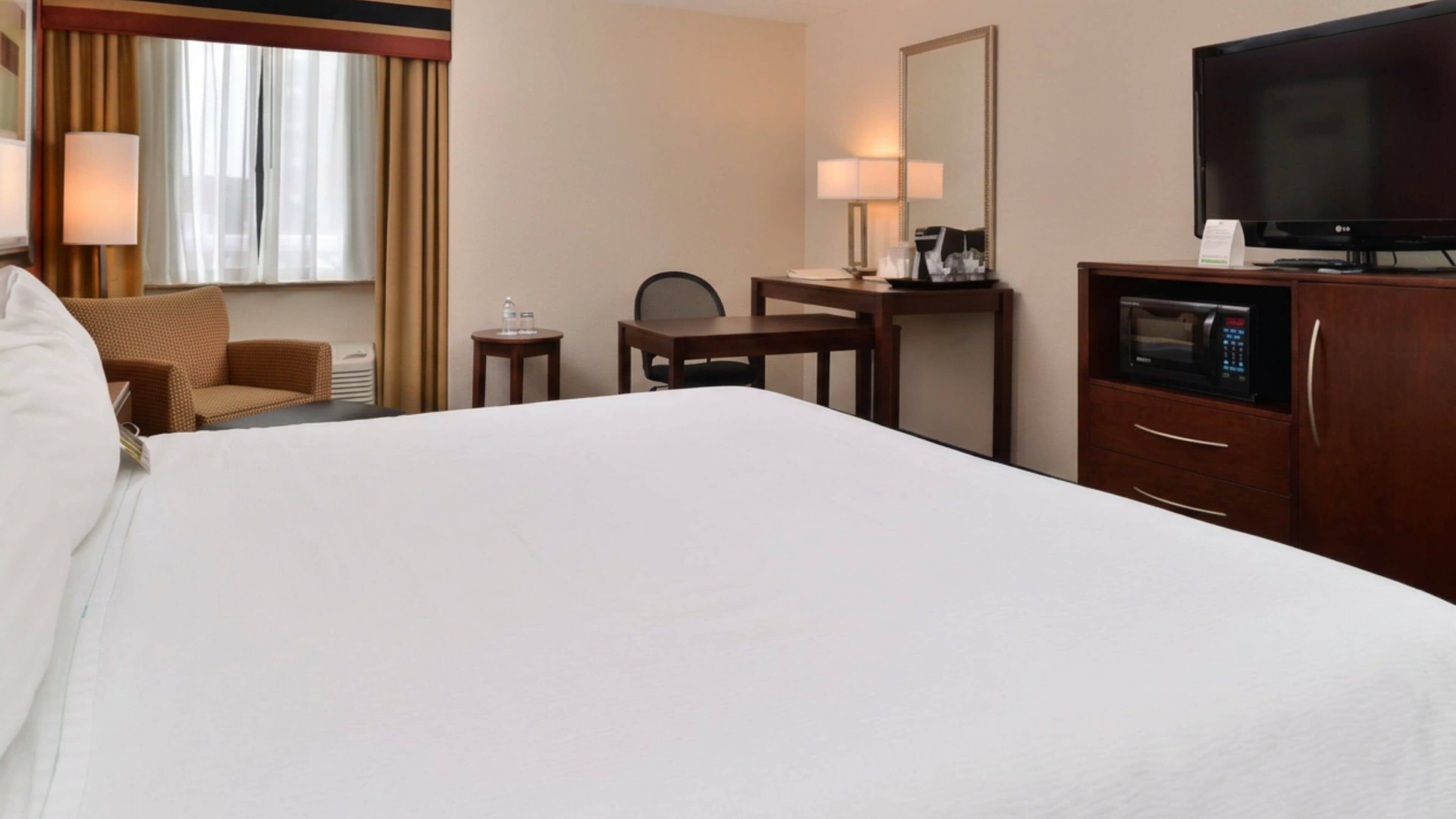 A hotel room with a large bed, a desk, a chair, a television, and a microwave.