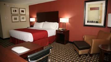 A hotel room with a large bed, a desk, a chair, a small table, and a wall-mounted telephone.
