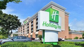 A Holiday Inn hotel with a prominent green and white sign, multiple floors, and a parking lot with cars. - Holiday Inn New London - Mystic Area by IHG (New London)