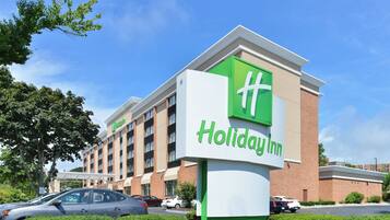 A Holiday Inn hotel with a prominent green and white sign, multiple floors, and a parking lot with cars.
