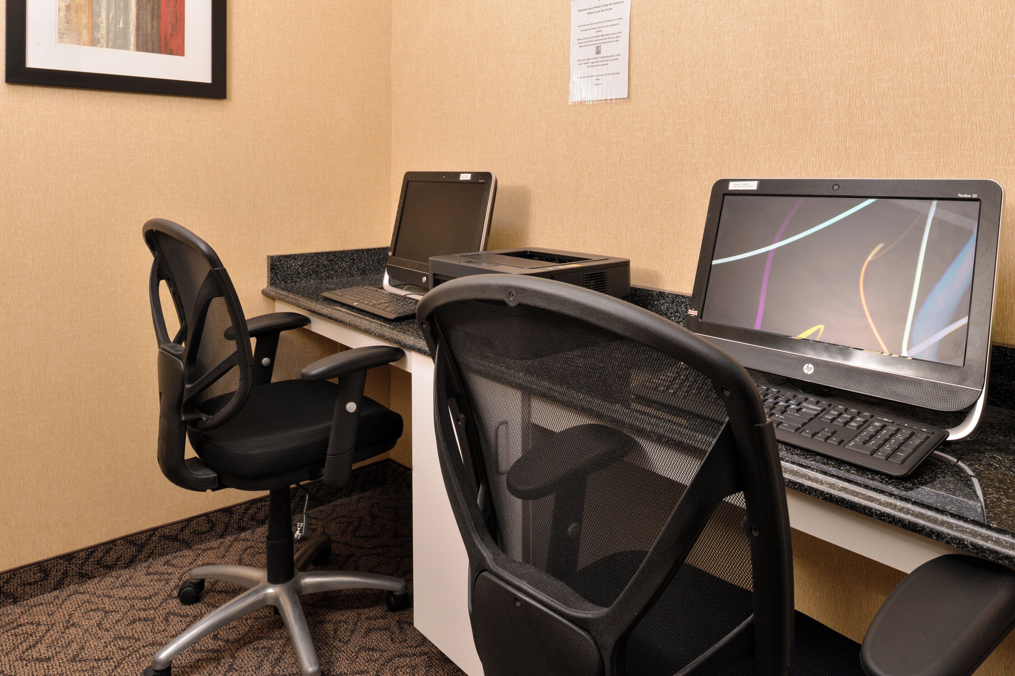 A hotel workspace with two HP laptops, a printer, and two office chairs.