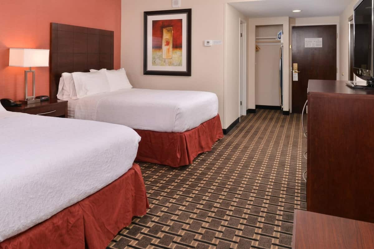A hotel room with two beds, a desk, a TV, and a framed picture on the wall.