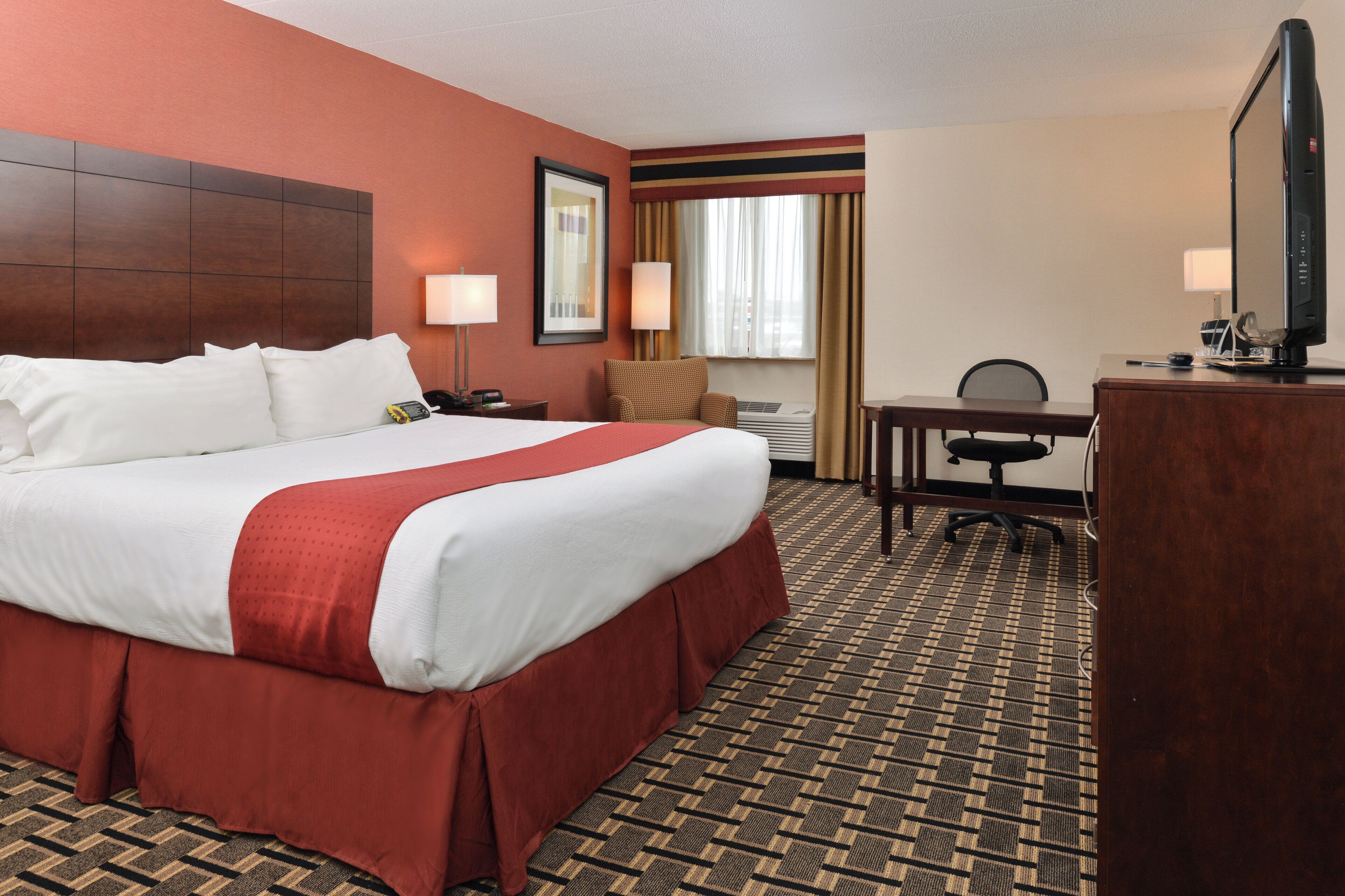 A hotel room with a large bed, a desk, a chair, a television, and a window with curtains.