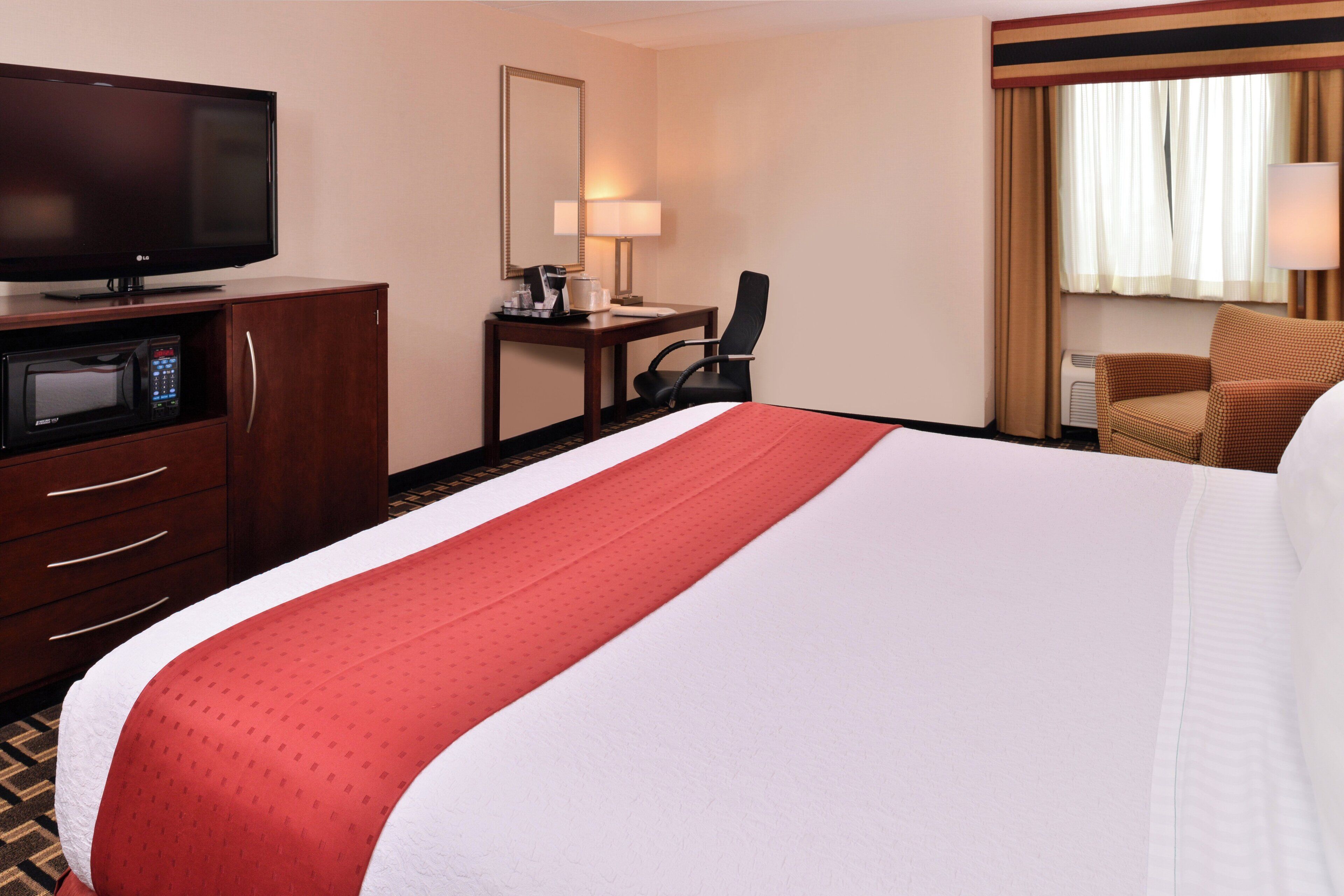 A hotel room with a bed, a desk, a chair, a television, and a microwave.