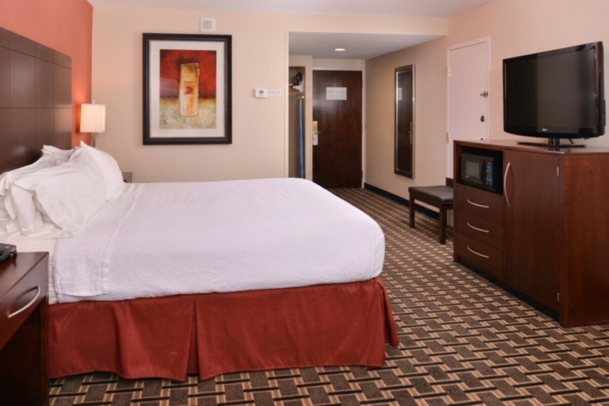 A hotel room with a bed, a desk with a telephone, a television, a wardrobe, and a framed picture on the wall.