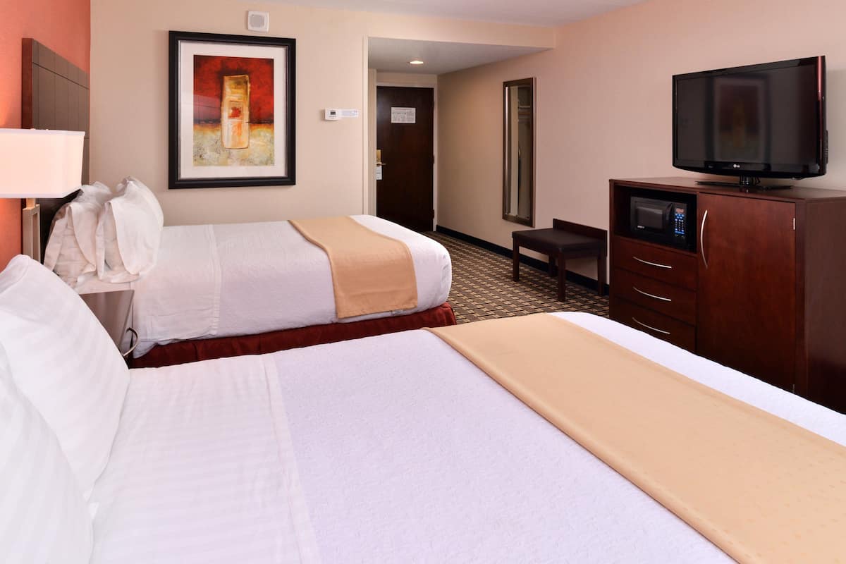A hotel room with two beds, a television, a microwave, and a desk.