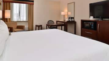 A hotel room with a large bed, a desk, a chair, a television, and a microwave.
