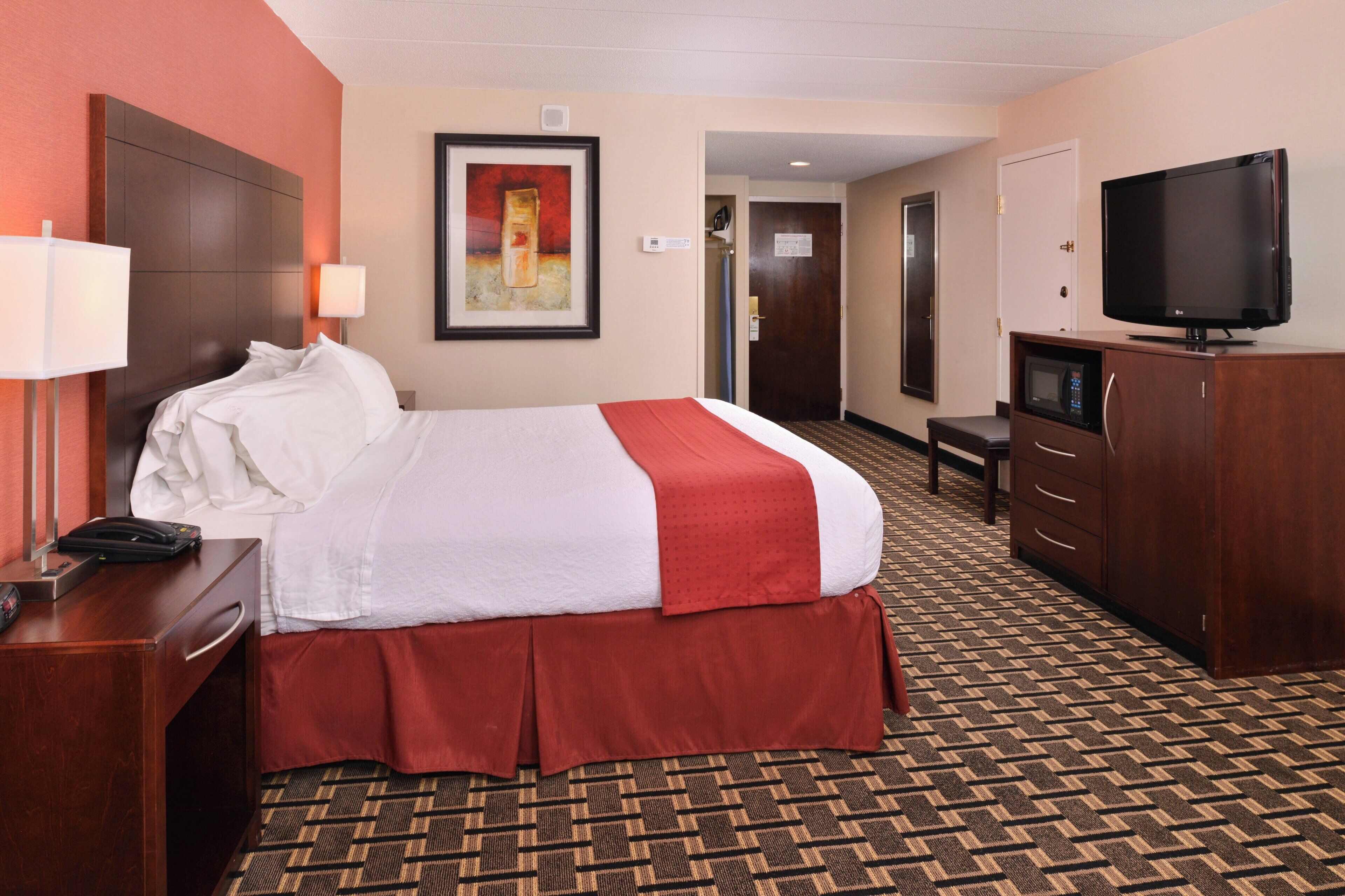 Una habitación de hotel con una cama, un escritorio con teléfono, televisión y microondas.