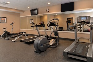 Un gimnasio con cintas de correr, elípticas y una banca para pesas.