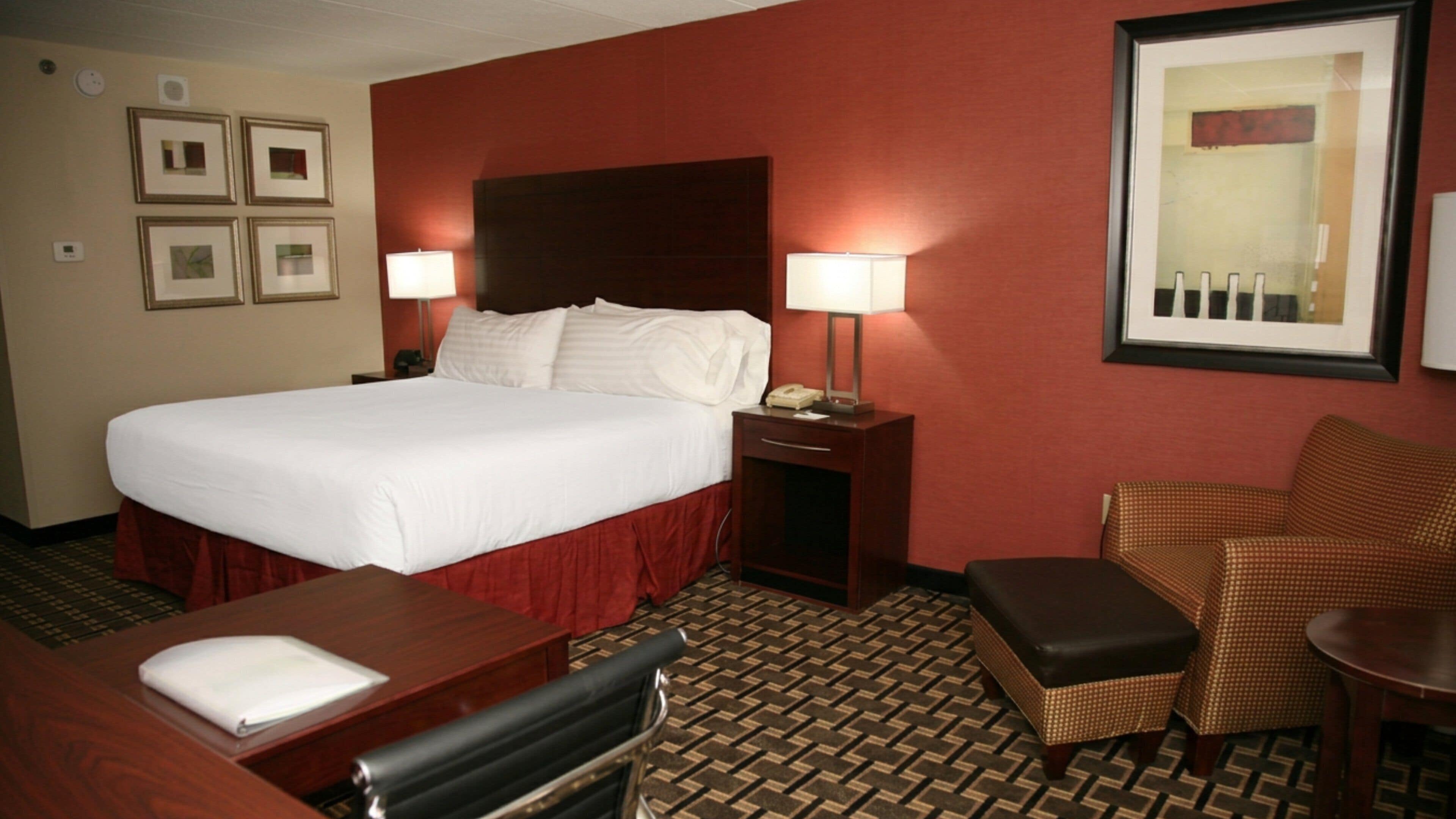 A hotel room with a large bed, two bedside tables, a desk, a chair, and a patterned carpet.
