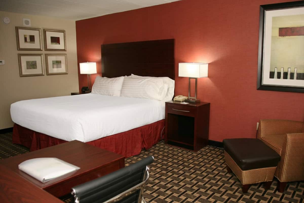 A hotel room with a large bed, two bedside tables, a desk, a chair, and a patterned carpet.