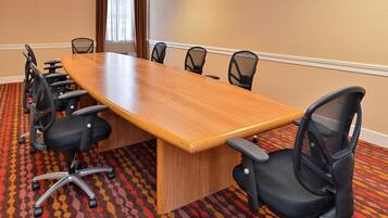Une salle de conférence avec une longue table en bois, entourée de chaises de bureau noires, un sol recouvert de moquette et des murs de couleur beige.