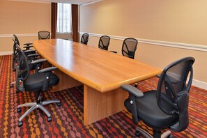 A conference room with a long wooden table surrounded by black office chairs, carpeted floor, and beige walls. - Holiday Inn New London - Mystic Area by IHG (New London)